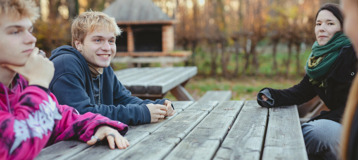 Drei Jugendliche sitzen gemeinsam im Freien an einem Holztisch
