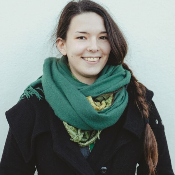 Eine junge Frau mit braunen langen Haaren und einem grünen Schal